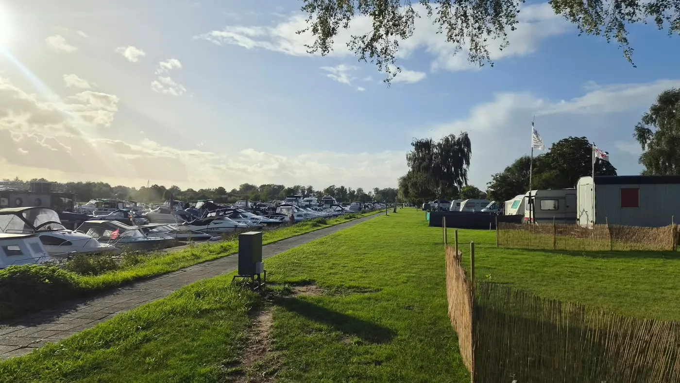 Der Weg auf dem Damm zwischen den Booten im Hafenbecken und der Stellplatzwiese