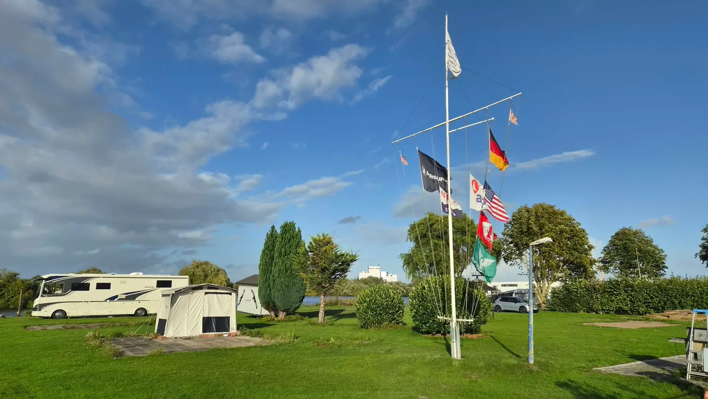 Der Flaggenmast auf der Stellplatzwiese, links ein Wohnmobil mit Vorzelt