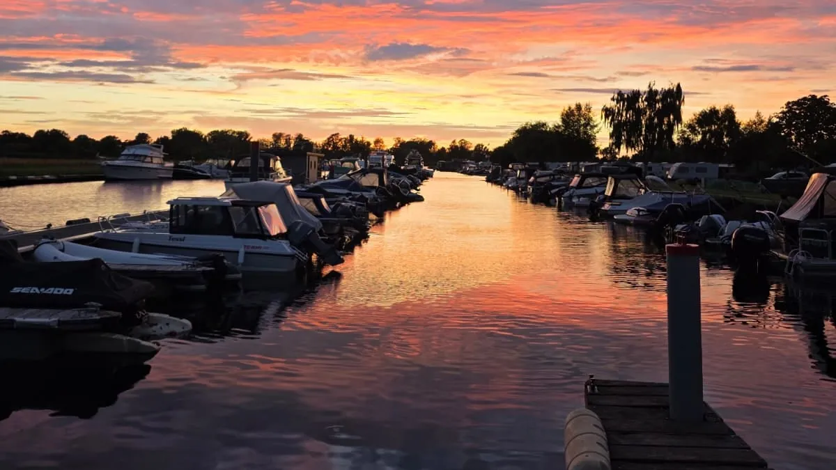 Sonnenuntergang über dem Hafenbecken: der rosa und orange Himmel spiegelt sich im Wasser zwischen den Bootsreihen, vorn rechts ein Holzsteg