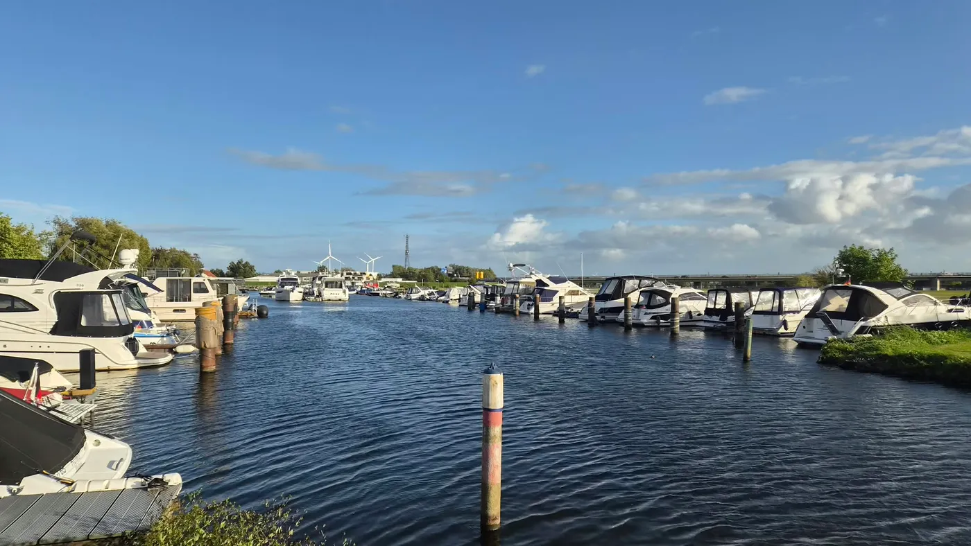 Blick über das Hafenbecken: an beiden Seiten liegen Motorboote am Steg, in der Mitte ragt ein Dalben aus dem Wasser