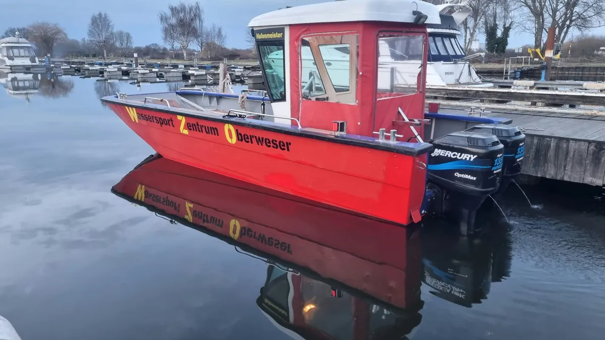 Das rote Hafenboot mit der Aufschrift „Wassersport Zentrum Oberweser“ liegt am Steg und spiegelt sich im stillen Wasser des Hafenbeckens