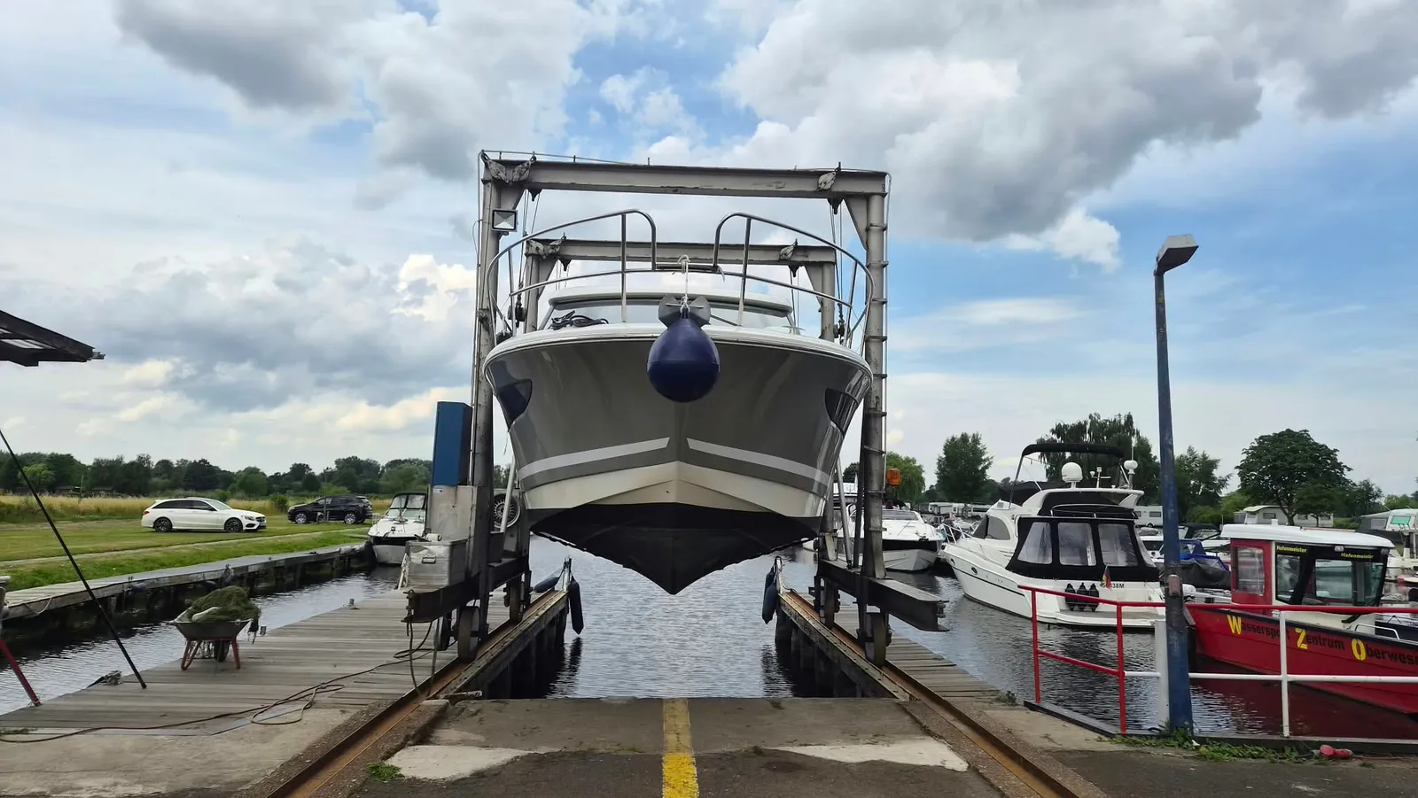 Der Hafenlift hebt eine Motoryacht in Gurten über der Gleisanlage aus dem Wasser