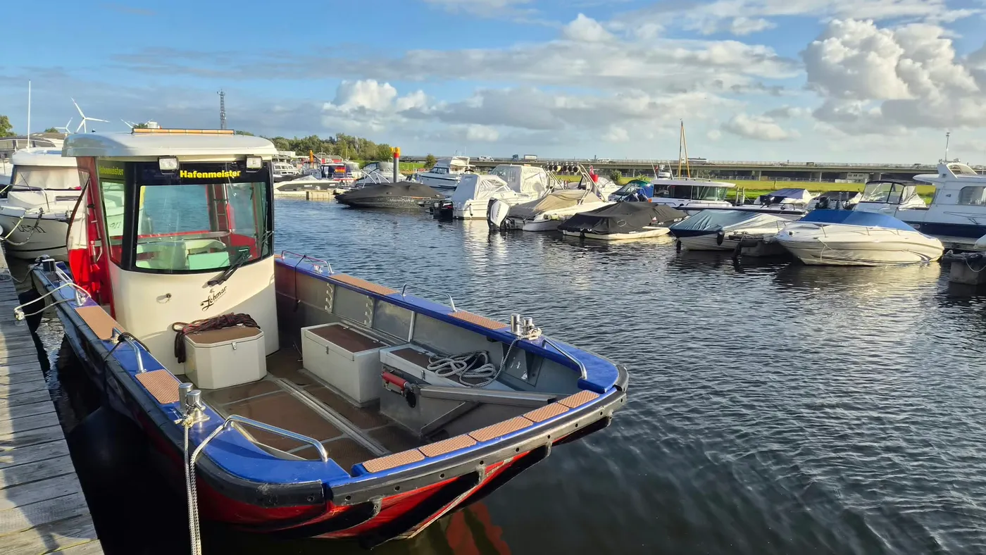 Das blau-rote Boot des Hafenmeisters liegt am Steg, dahinter die Liegeplätze im Hafenbecken
