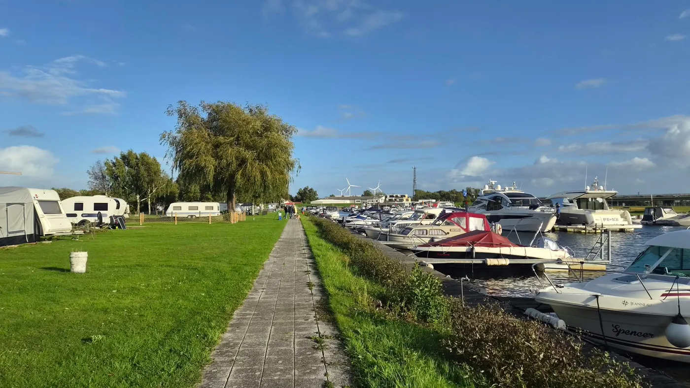 Plattenweg zwischen der Stellplatzwiese mit Wohnwagen und den Booten am Steg, in der Mitte eine große Weide