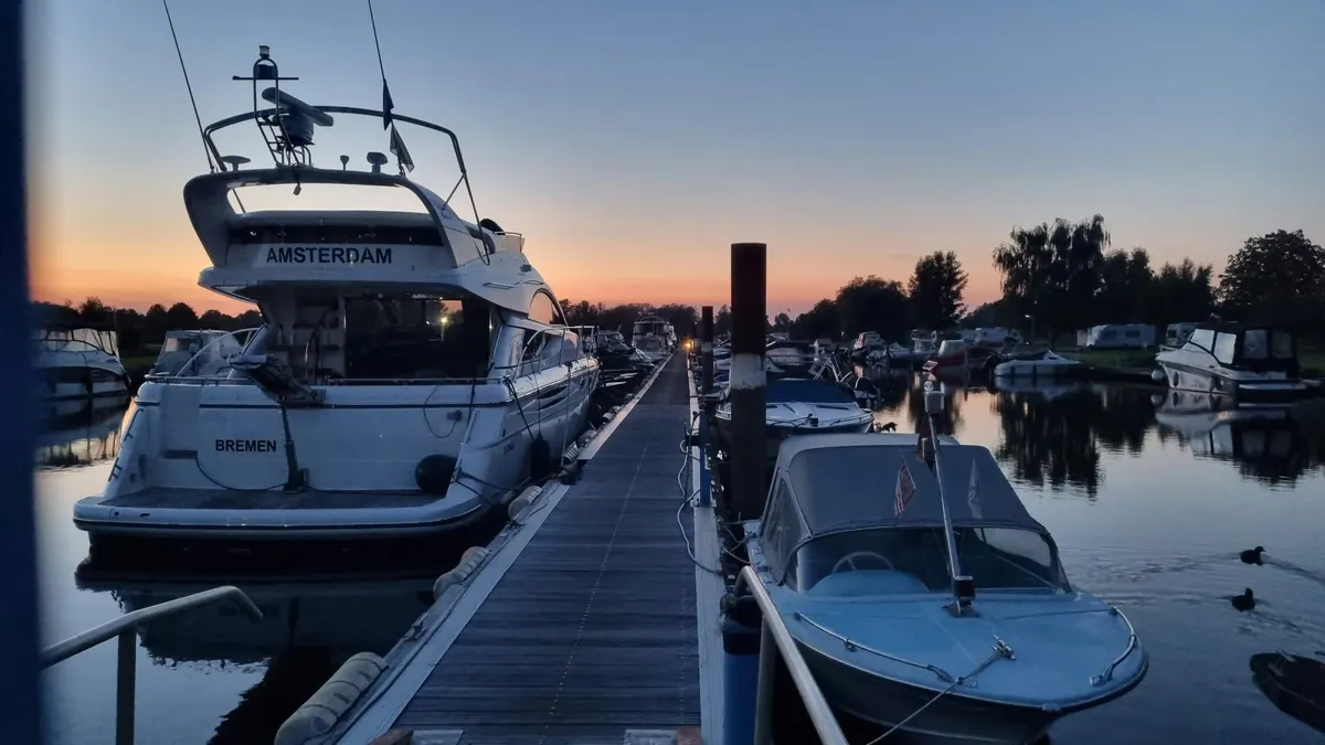 Steg zwischen zwei Bootsreihen am Abend, links eine Motoryacht, rechts ein offenes Sportboot