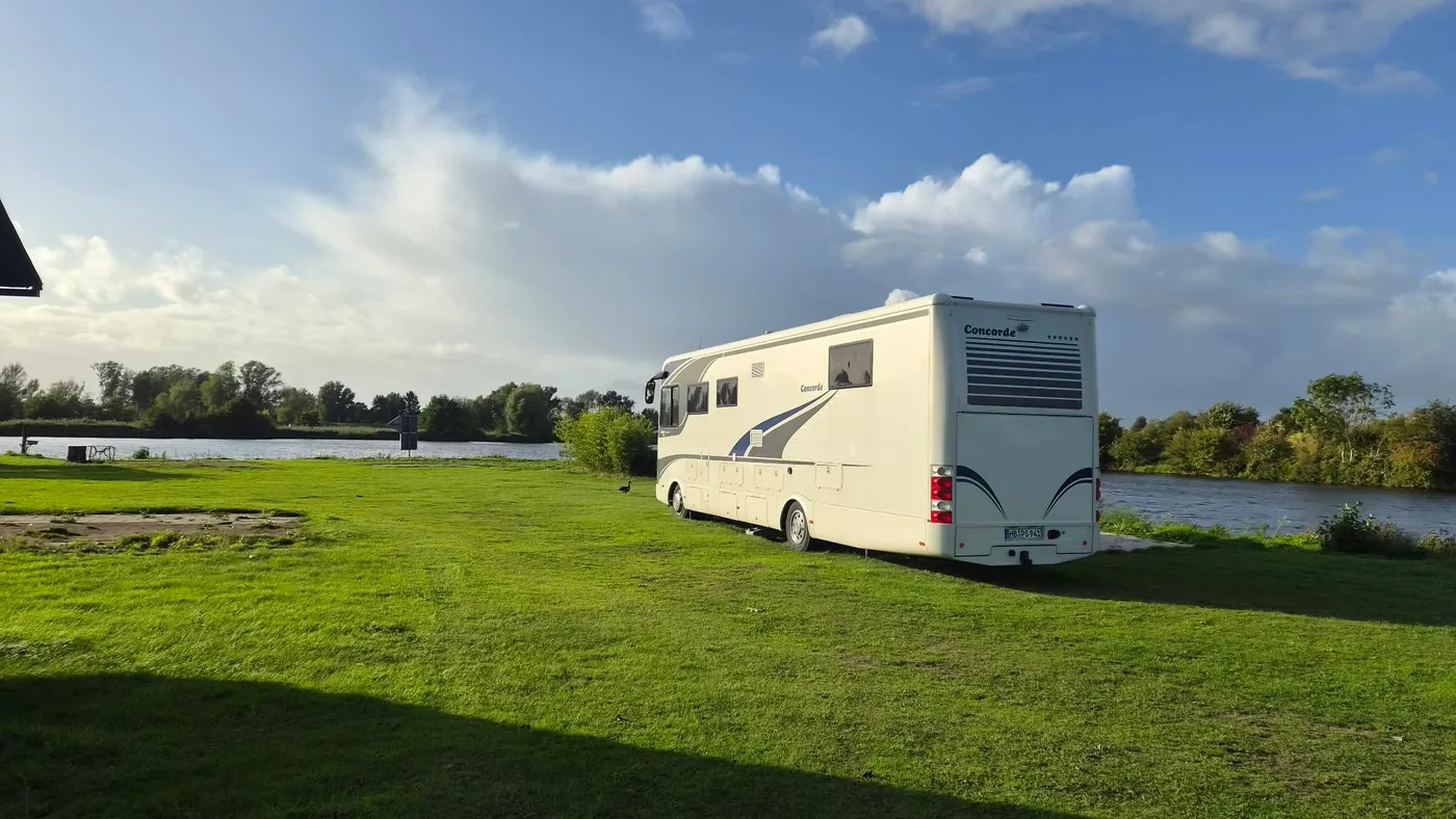 Ein großes Wohnmobil steht allein auf der Stellplatzwiese unmittelbar am Weserufer